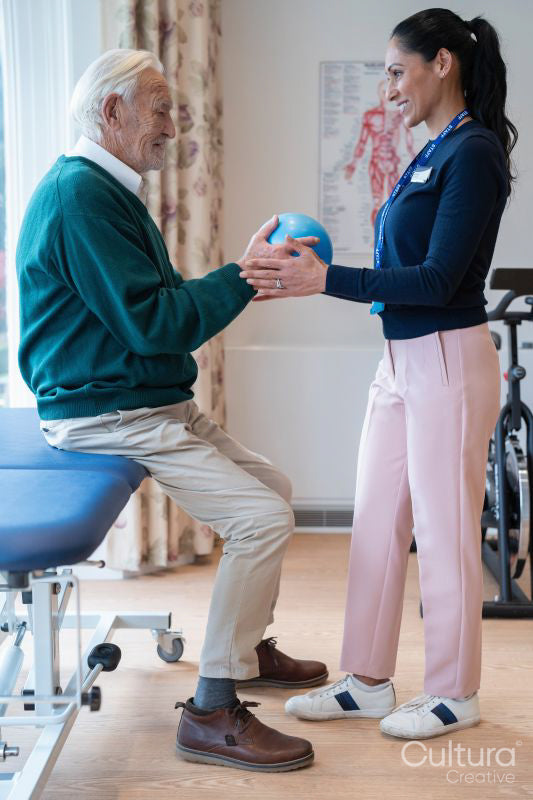 Smiling female therapist assisting senior man exercising with ball