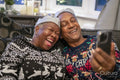 Senior couple sitting on sofa wearing Christmas decorations and using phone