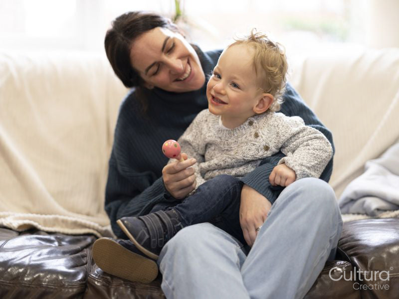 Son with cerebral palsy sitting on mothers lap on sofa