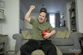 Man sitting on sofa, holding soccer ball and cheering