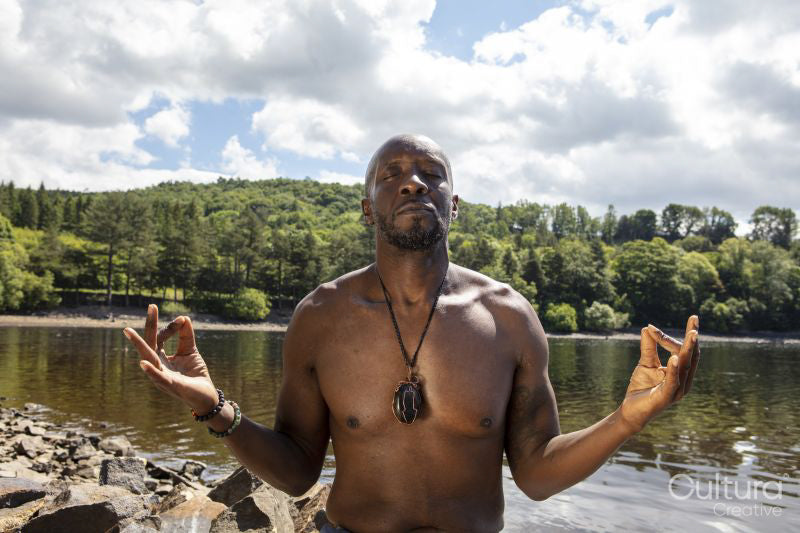 Shirtless man meditating on lakeshore, Yorkshire, UK