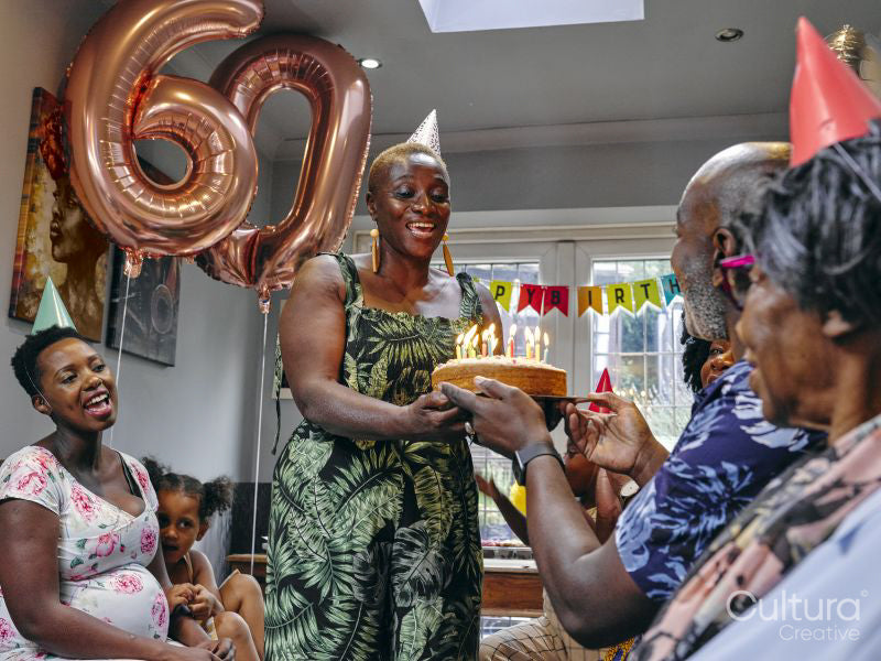 Woman giving man birthday cake at birthday party with family