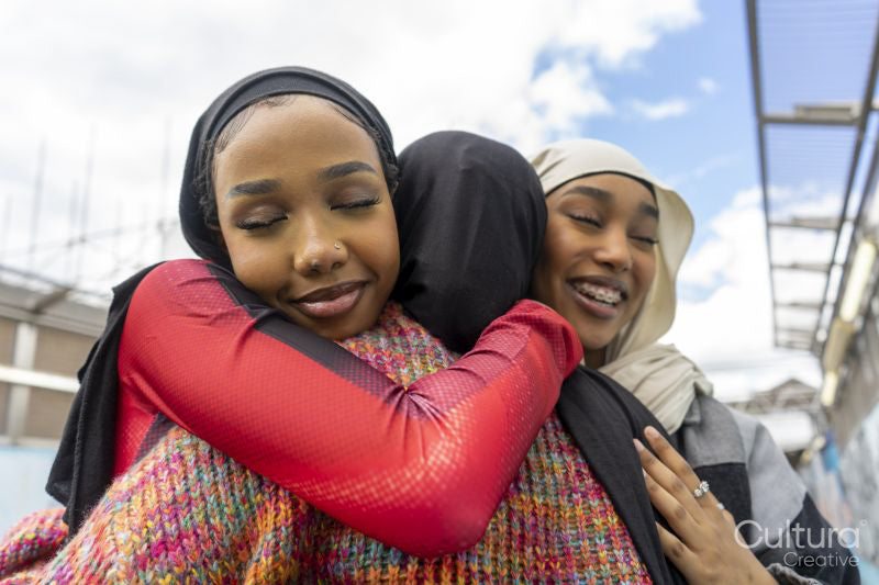 Young women wearing hijabs hugging in city