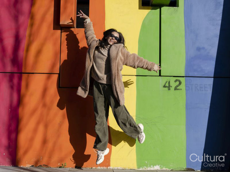 Portrait of young woman jumping in front of colorful graffiti wall