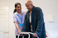 Nurse helping senior man to walk with mobility walker at nursing home