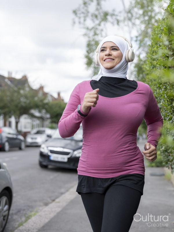Sutton,Woman in headscarf and headphones jogging on sidewalk
