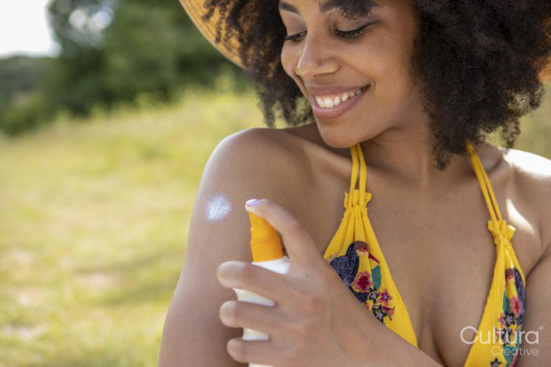 Young woman wearing summer hat applying suntan lotion