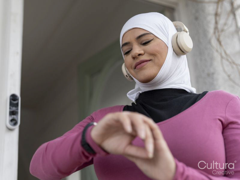Sutton,Woman in headscarf and headphones checking smart watch