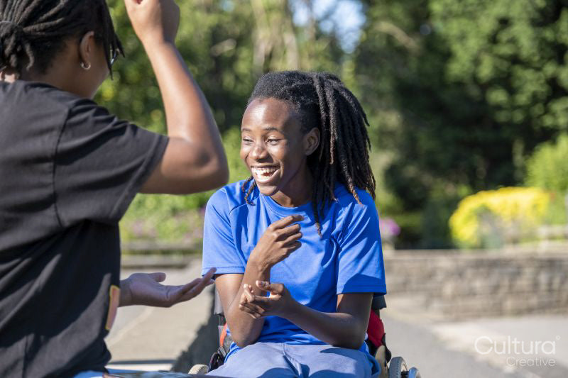 Teenage girl in wheelchair with friend playing in park