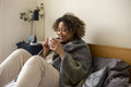 Smiling woman wrapped in shawl holding cup on bed