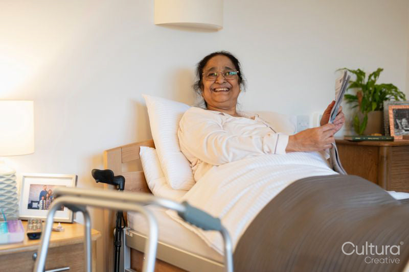 Senior lady reading newspaper in bed at nursing home