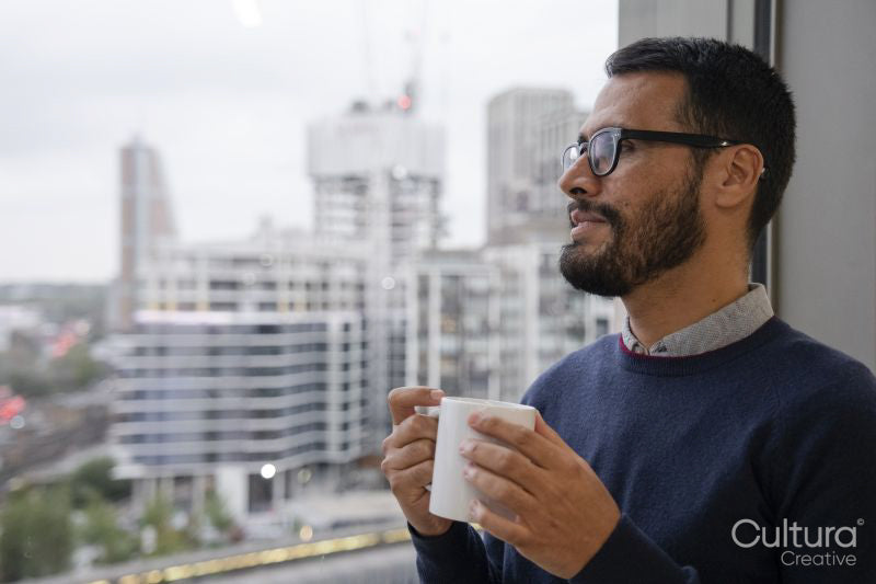 Man with coffee mug looking out window