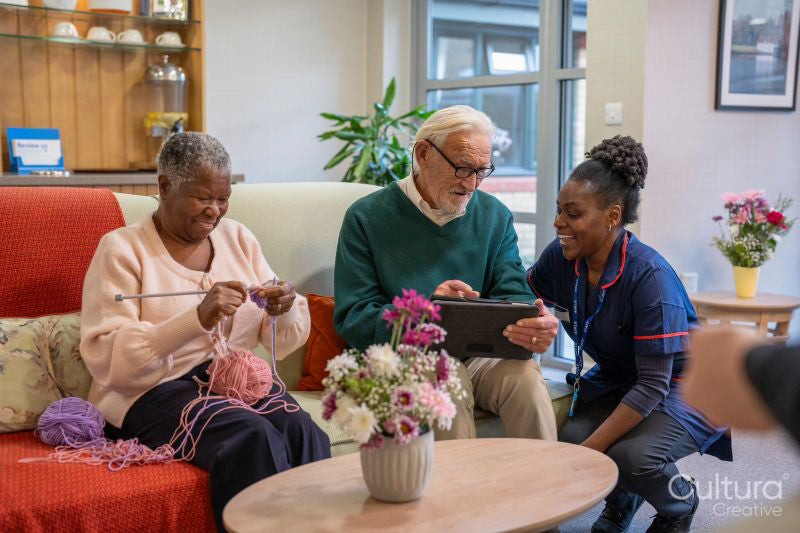 Smiling nurse helping senior man use tablet in nursing home