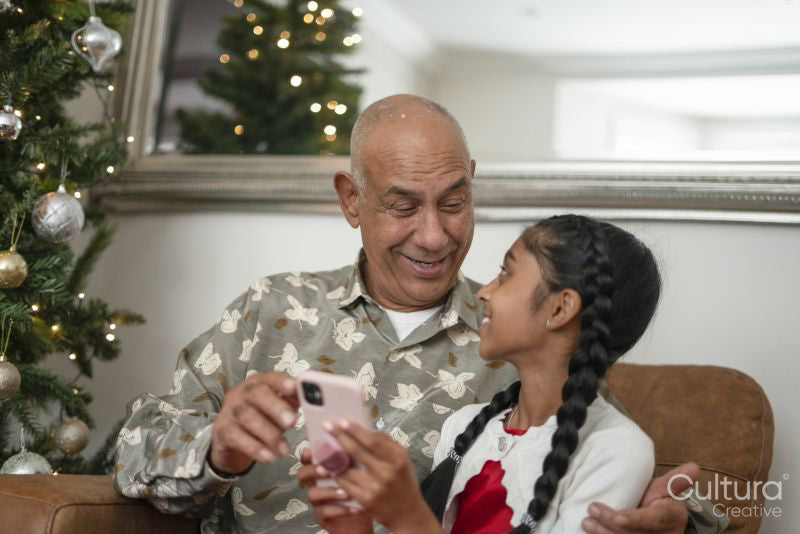 Senior man with granddaughter looking at smart phone at Christmas tree
