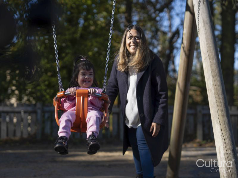Mother swinging daughter with Down syndrome on playground swing