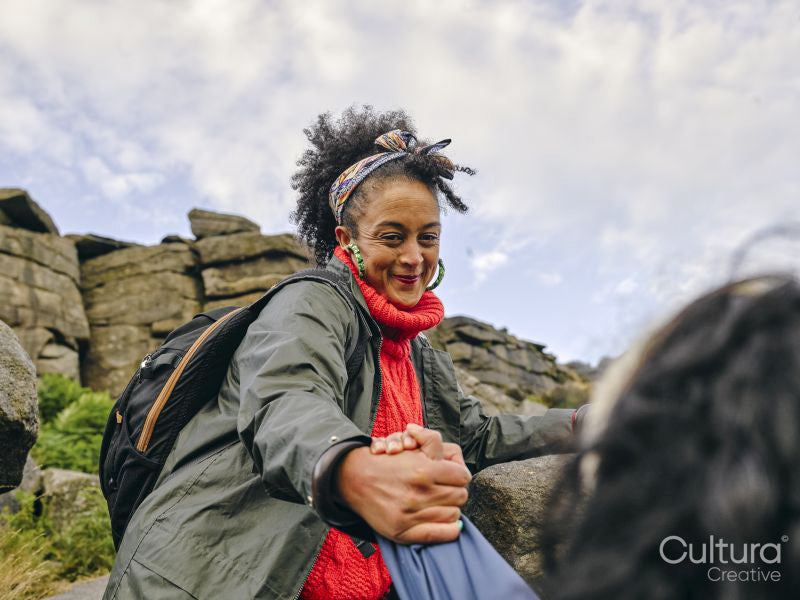 Woman helping fellow hiker climb rocky mountain