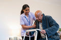 Nurse helping senior man to stand up with mobility walker at nursing home