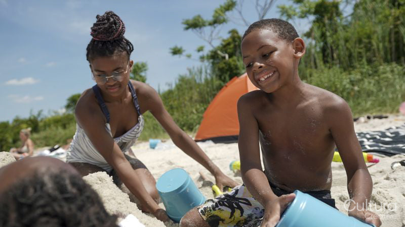 Brother and sister covering father with sand on beach