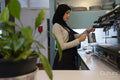 Young woman in hijab making coffee in cafe