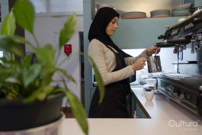 Young woman in hijab making coffee in cafe
