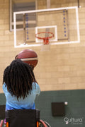 Teenage girl in wheelchair shooting ball on basketball court