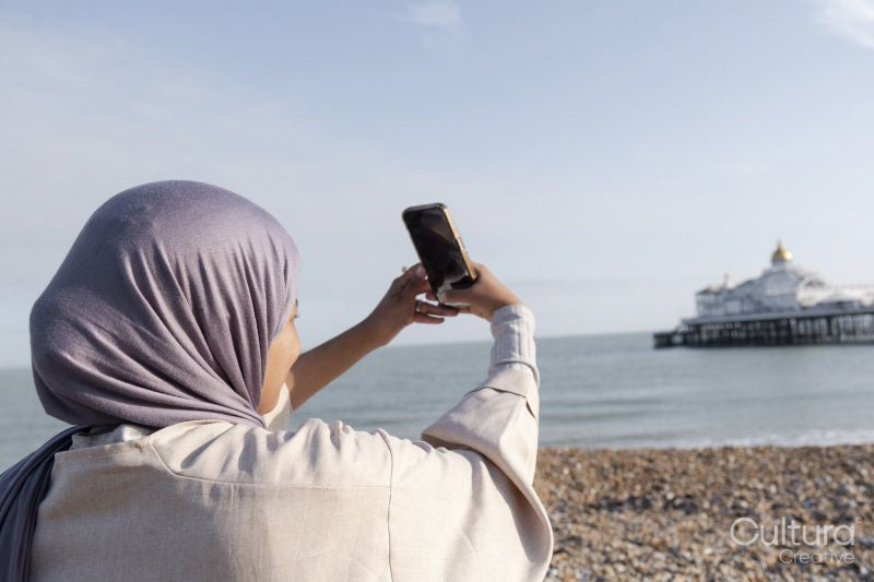 Muslim woman taking selfie by sea on sunny day