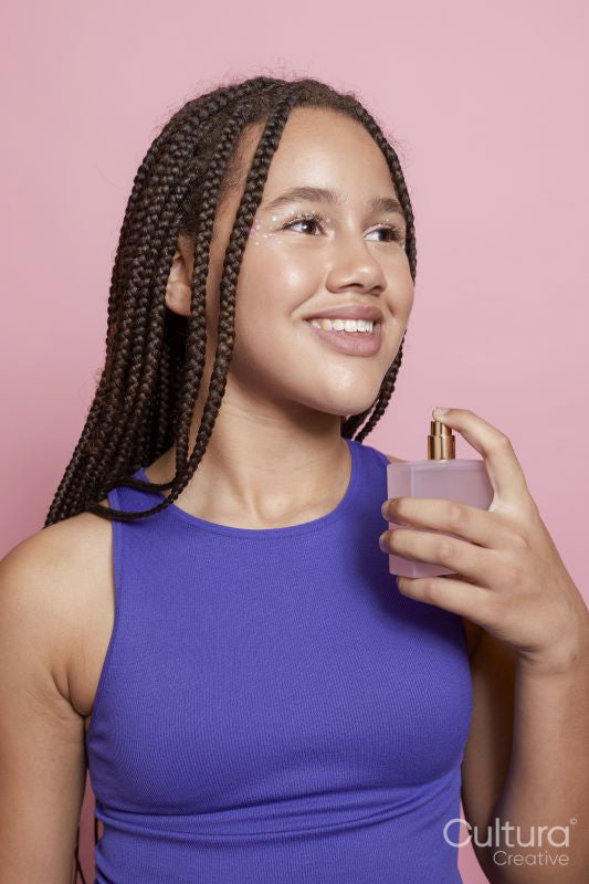 Studio portrait of smiling girl spraying perfumes on neck