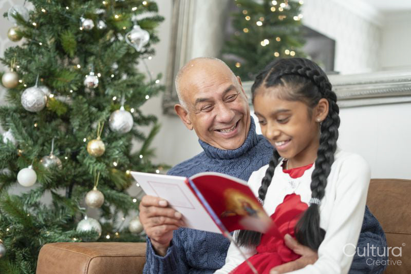 Senior man with granddaughter reading book at Christmas tree