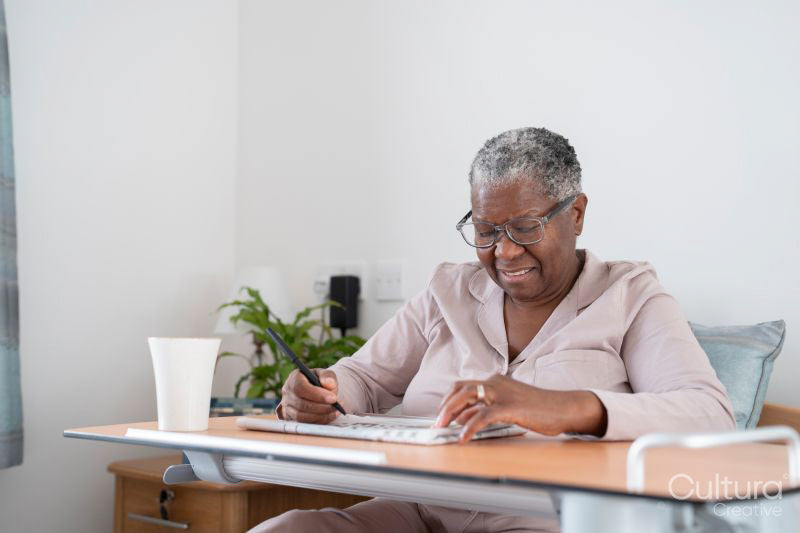 Smiling senior woman in bathrobe sitting on bed and doing crossword puzzle in nursing home