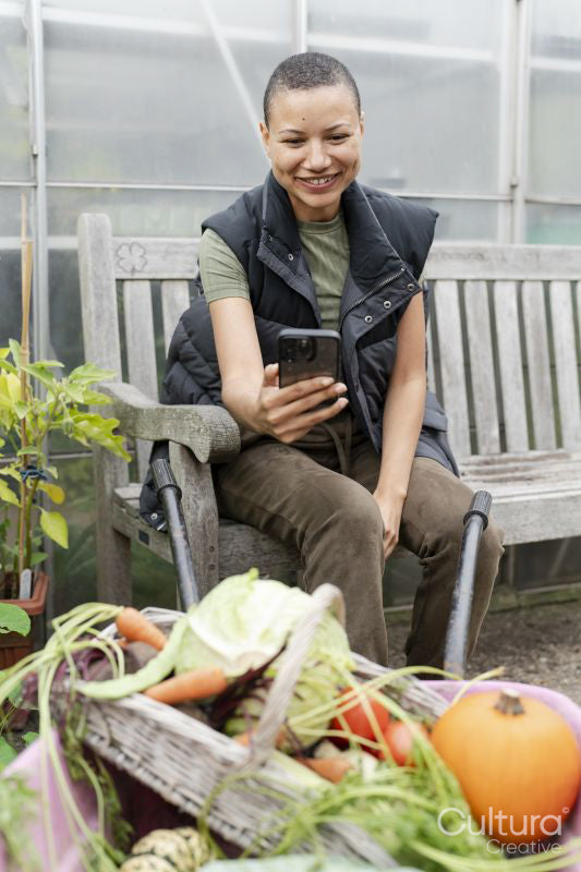 Smiling woman photographing harvested vegetables with smart phone