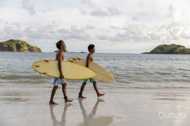Indonesia, Lombok, Side view of two surfers walking with surfboards on beach