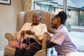 Smiling nurse looking at senior woman knitting in nursing home