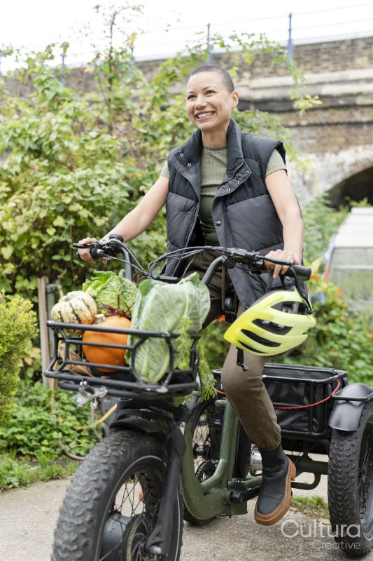 Smiling woman riding cargo electric trike loaded with homegrown vegetables