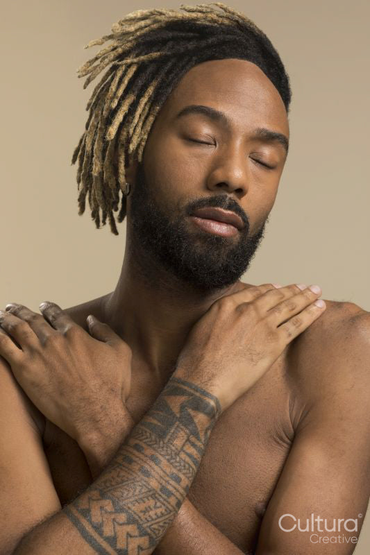 Studio shot of young man with dreadlocks hugging self