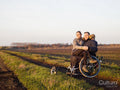 Smiling man on wheelchair in field with woman on laps