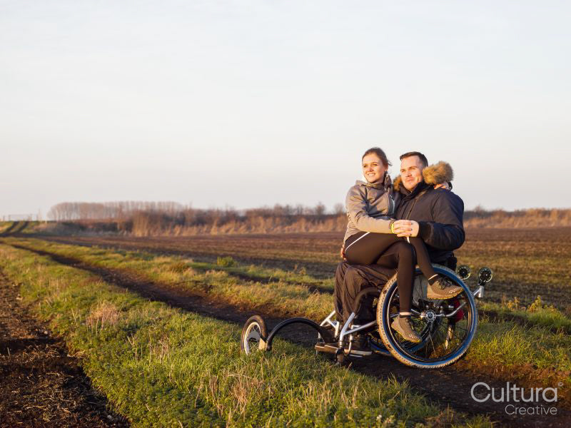 Smiling man on wheelchair in field with woman on laps