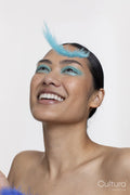 Smiling woman wearing blue makeup looking at falling feather