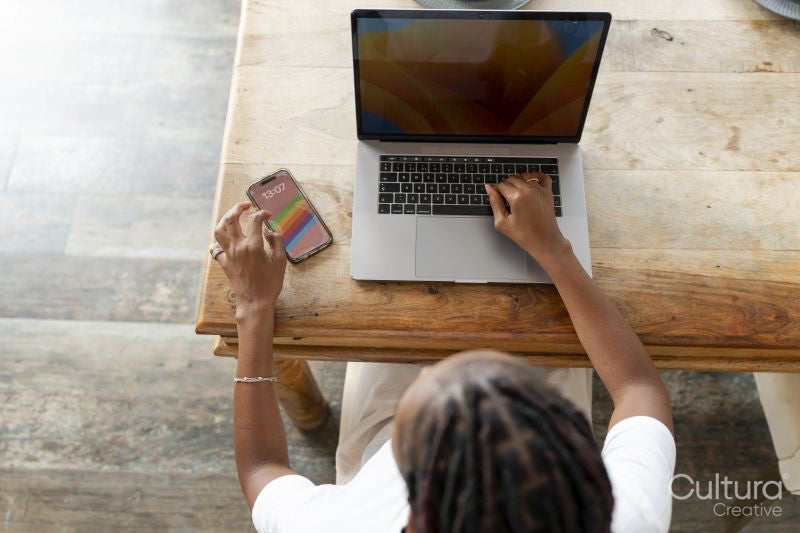 Young woman using smart phone while working on laptop at home