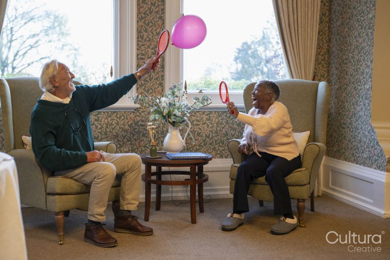 Smiling senior man and woman playing with balloon in nursing home