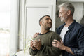 Mature male couple standing by window at home