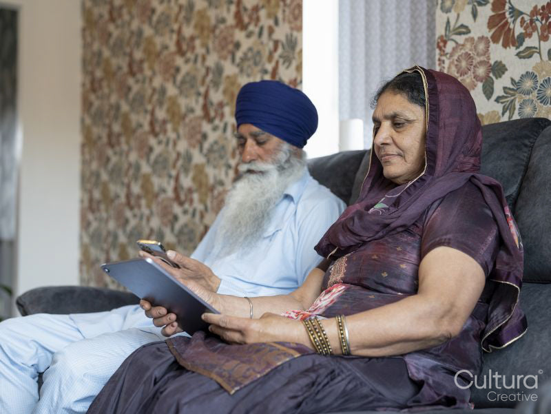 Senior couple in traditional clothing using phone and tablet at home