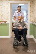 Female care giver pushing senior man in wheelchair in nursing home