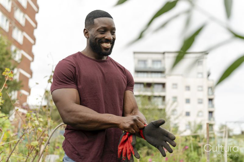 Smiling man putting on gloves in urban vegetable garden