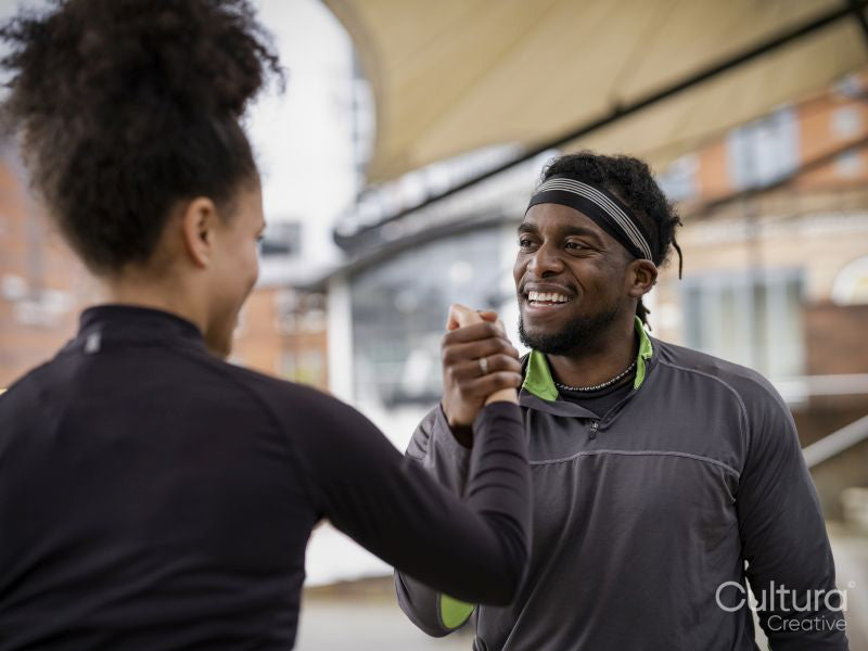 Smiling man and woman in sports clothing arm wrestling outdoors