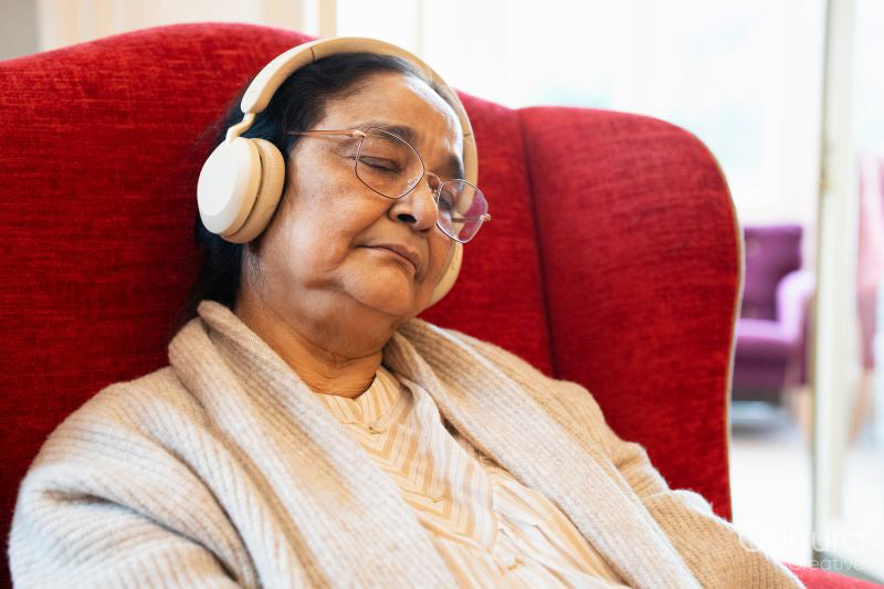 Senior woman using headphones, sitting in armchair and napping