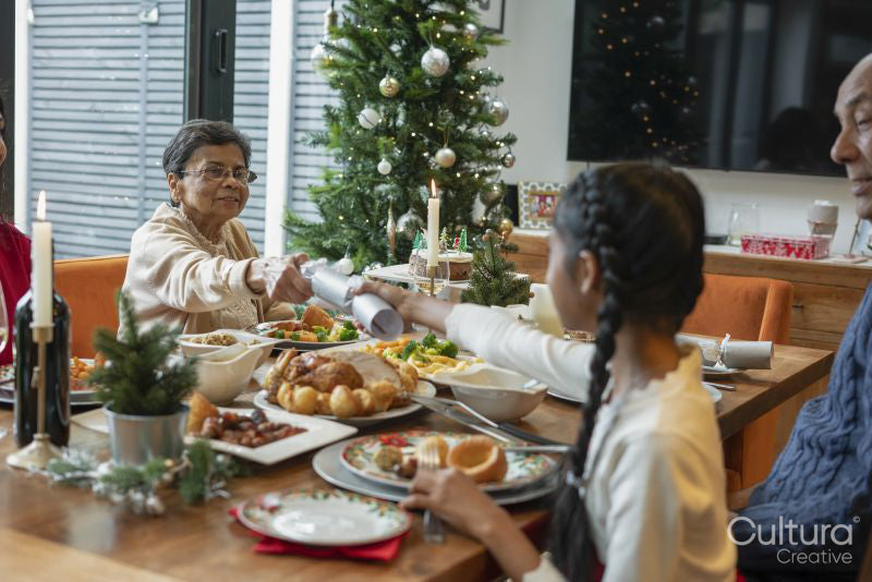 Girl with grandmother holding Christmas cracker across table