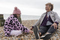 Grandmother and granddaughter sitting on beach on cloudy day