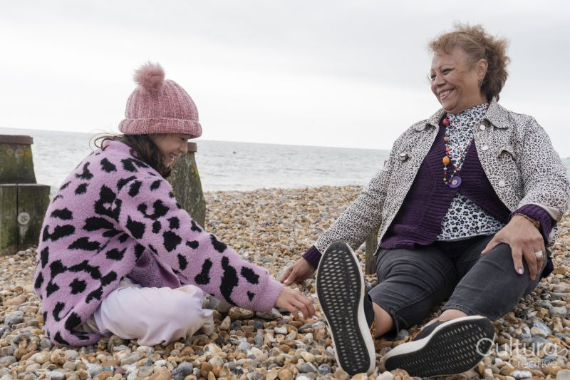 Grandmother and granddaughter sitting on beach on cloudy day