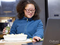 Girl with Down Syndrome using laptop and preparing food in kitchen