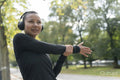 Woman in headphones and sports clothing stretching arm in park